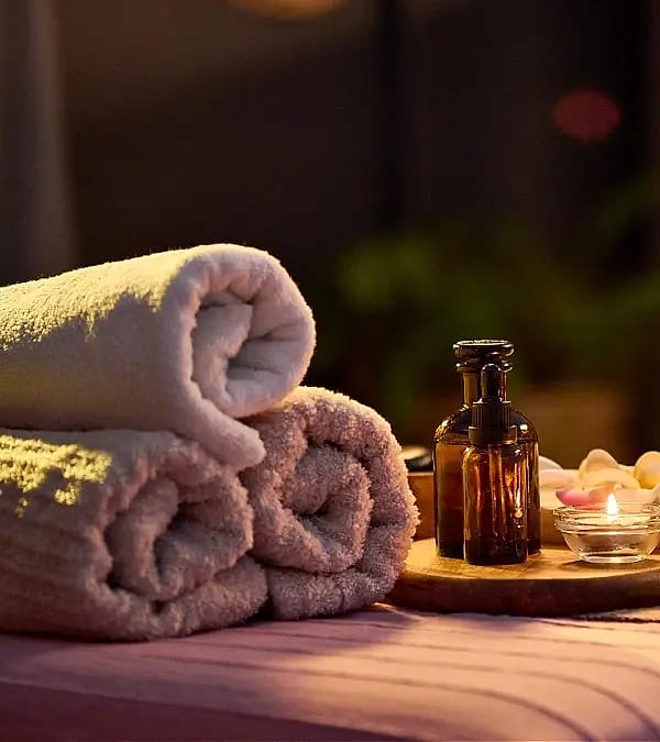 Rolled towels, massage oil and a candle on a treatment bed